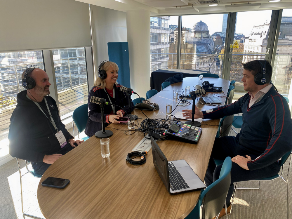 Three people are seated around a table in an office setting recording a podcast